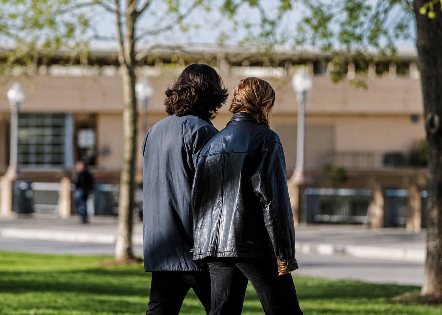 A man and a woman walking together through a park, seen from behind